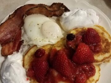 Breakfast with pancakes topped with strawberries, egg and bacon