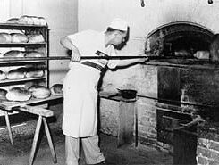 man putting bread in brick oven